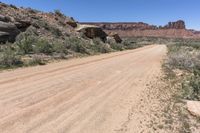 a dirt road near some cliffs and brushs with no cars in sight on it