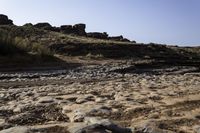 a view of a rocky beach with an open fire hydrant in the distance, and lots of dry grass