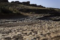 a view of a rocky beach with an open fire hydrant in the distance, and lots of dry grass