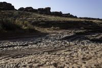 a view of a rocky beach with an open fire hydrant in the distance, and lots of dry grass