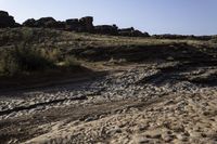 a view of a rocky beach with an open fire hydrant in the distance, and lots of dry grass