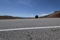 the empty desert road is surrounded by mountains and low hills, on a bright sunny day