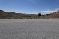 the empty desert road is surrounded by mountains and low hills, on a bright sunny day