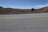 the empty desert road is surrounded by mountains and low hills, on a bright sunny day