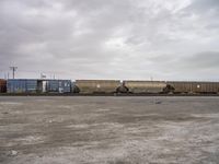 a train carrying containers is parked on the tracks in a parking lot, and it's cloudy