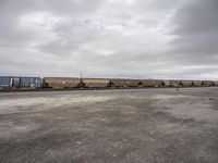 a train carrying containers is parked on the tracks in a parking lot, and it's cloudy