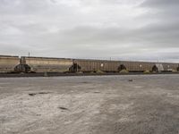 a train carrying containers is parked on the tracks in a parking lot, and it's cloudy