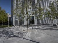 a lone bench and several trees against a backdrop of a building with multiple windows and tall steel mesh doors