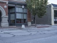 the empty city street with a tall brick building on the corner and parking meter near by