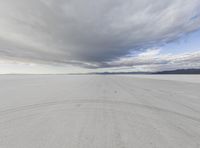 an open desert with tracks in the sand under dark clouds and blue skies above a lone street and hills