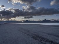 a large body of water sitting under cloudy skies next to a mountain range under a cloudy sky