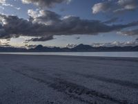 a large body of water sitting under cloudy skies next to a mountain range under a cloudy sky