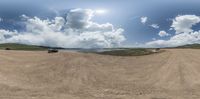 a car drives through a dirt plain toward water in the distance is a mountain and some clouds