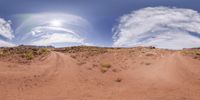 dirt road through sand dunes and mountains with wispy clouds above them in daytime