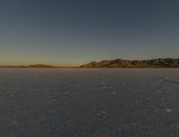 a lone person in a snow covered desert with mountains in the distance and blue sky