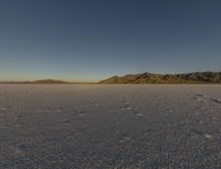 a lone person in a snow covered desert with mountains in the distance and blue sky