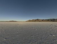 a barren landscape with mountains in the background and footprints imprints on the sand under a clear blue sky