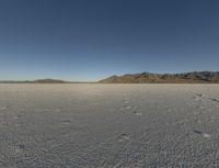 a barren landscape with mountains in the background and footprints imprints on the sand under a clear blue sky