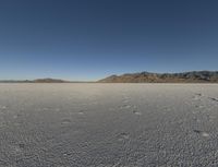 a barren landscape with mountains in the background and footprints imprints on the sand under a clear blue sky