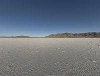 a barren landscape with mountains in the background and footprints imprints on the sand under a clear blue sky