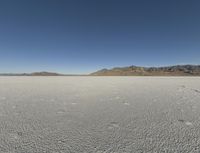 a barren landscape with mountains in the background and footprints imprints on the sand under a clear blue sky