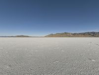 a barren landscape with mountains in the background and footprints imprints on the sand under a clear blue sky