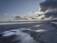 sunset behind storm clouds over an empty beach area with puddles of water and concrete