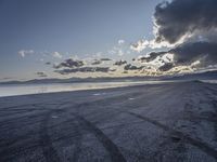 sunset behind storm clouds over an empty beach area with puddles of water and concrete