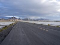 a paved road running along an empty field in the middle of nowhere with mountains behind it