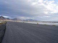 a paved road running along an empty field in the middle of nowhere with mountains behind it