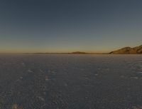 a large area of empty snow with mountains in the distance behind it and a sky background