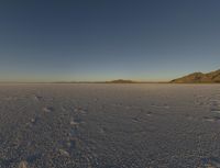 a large area of empty snow with mountains in the distance behind it and a sky background