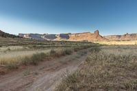 a dirt path winds through the field near tall rock formations in the distance are a mountain range