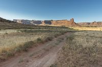 a dirt path winds through the field near tall rock formations in the distance are a mountain range