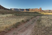 a dirt path winds through the field near tall rock formations in the distance are a mountain range