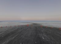 orange cones are sitting in the middle of a plain of snow and dirt, and a stop sign in the middle