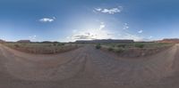 a 360 - view image of dirt road in the middle of desert landscape with sun shining over hill