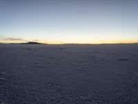 a lone snowboarder walks across the snow at sunset on an empty plain of snow