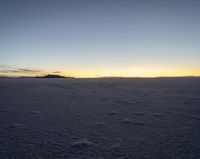 a lone snowboarder walks across the snow at sunset on an empty plain of snow