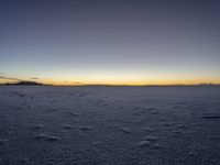 a lone snowboarder walks across the snow at sunset on an empty plain of snow