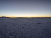 a lone snowboarder walks across the snow at sunset on an empty plain of snow