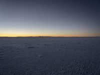 a lone snowboarder walks across the snow at sunset on an empty plain of snow