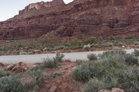 a person on a motorcycle rides down a road in front of mountains, and shrubs