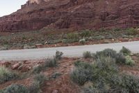 a person on a motorcycle rides down a road in front of mountains, and shrubs