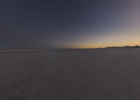 an orange sunset shines over an empty desert plain and mountains on the horizon,