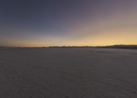 an orange sunset shines over an empty desert plain and mountains on the horizon,