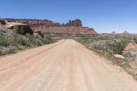 an empty dirt road in the middle of a desert mountain side area of rocks and scrubs with dirt