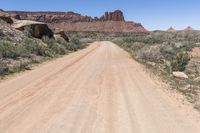 an empty dirt road in the middle of a desert mountain side area of rocks and scrubs with dirt