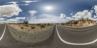 a 360 - angle picture of two curved road sections, and a large white cloud on the horizon, against the bright blue sky