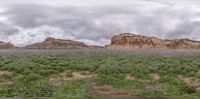 a group of green bushes and trees along side of a canyon near mountains with clouds